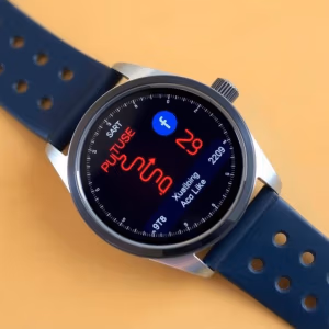 En pulsklocka.se smartwatch med blått armband visar hälsostatistik, inklusive "PUTUSE" och en hjärtfrekvens på 129, på sin runda svarta skärm. Bakgrunden är heltäckande ljusorange.