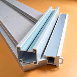 Tre aluminiumprofiler.se i olika former och storlekar vilar på en ljusorange yta och visar sina tvärsnitt och ihåliga insidor.