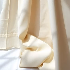 Mjukt krämfärgat tyg från linneduk.se draperas graciöst med naturligt ljus som kastar mjuka skuggor över vecken för en lugn och elegant look.