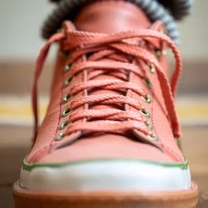 Närbild på en rosa sneaker från skosnören.se med vit och grön kant, snyggt snörad med synliga öljetter. Skons framsida och snörning är i fokus mot en suddig bakgrund.